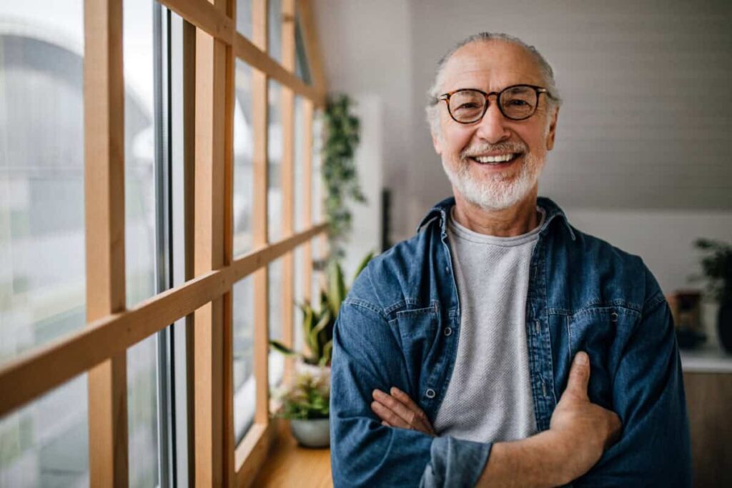 This Stock Pays You a 4.7% Dividend Every Single Month senior man smiles next to a light-filled window